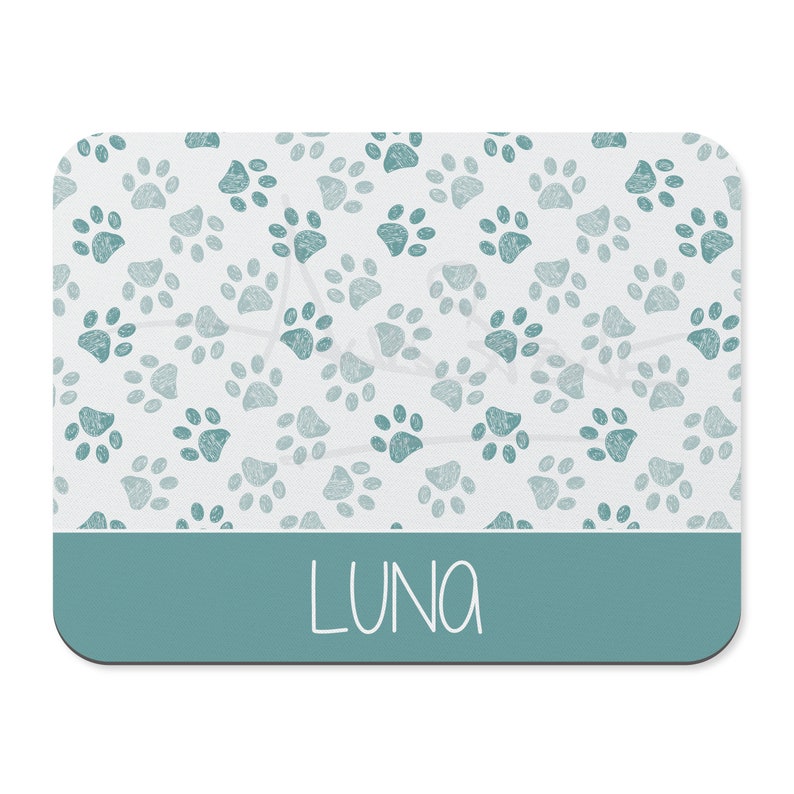 May include: A teal blue rectangular pet placemat with a white background and a pattern of teal blue paw prints. The name "LUNA" is written in white script at the bottom of the placemat.