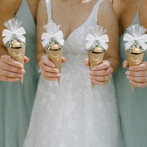 May include: Four women holding brown paper cone favors. Each cone is filled with small white flowers and a gold-wrapped chocolate. The cones are topped with white bows and cellophane. The words "Thank you!" are printed on each cone.