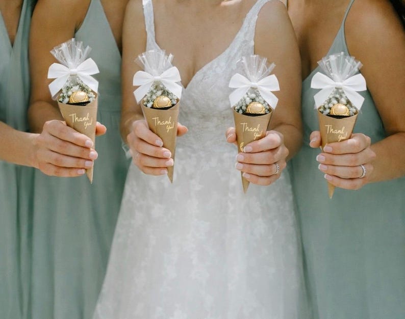 May include: Four women holding brown paper cone favors. Each cone is filled with small white flowers and a gold-wrapped chocolate. The cones are topped with white bows and cellophane. The words "Thank you!" are printed on each cone.