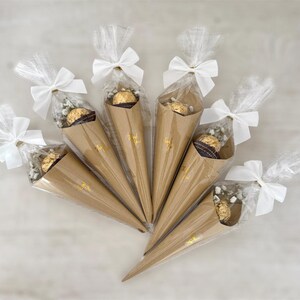 May include: Six cone-shaped party favors. Each favor is made of brown paper, filled with a chocolate candy and baby's breath, and wrapped in clear cellophane. White bows secure the cellophane. The words "Thank You" are printed in gold.