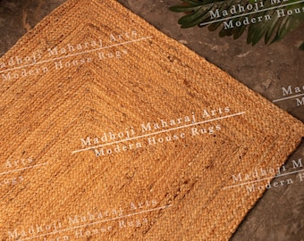 May include: A natural fiber rug made from jute, a sustainable and eco-friendly material. The rug is a light brown color and has a woven texture. The rug is rectangular and has a fringed edge. The rug is displayed on a gray tiled floor. The text "Madhoji Maharaj Arts Modern House Rugs" is printed on the rug.