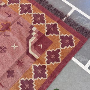 Könnte beinhalten: Ein rosafarbener und orangefarbener Teppich mit geometrischem Muster. Der Teppich hat einen Fransenrand.