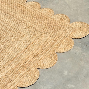 May include: A natural fibre rug with a scalloped edge. The rug is made of a woven material and is a light brown colour.