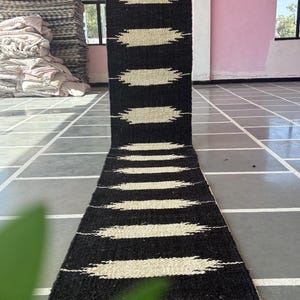 Könnte beinhalten: Schwarz-weißer gestreifter Teppich mit geometrischem Muster. Der Teppich ist aus Naturfasern gefertigt und hat einen rustikalen Look.