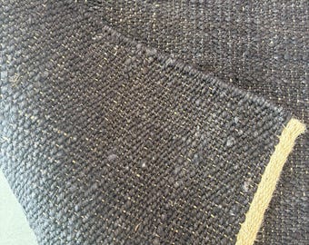 May include: Close-up of a black and tan woven rug with a textured surface. The rug has a subtle sheen and a slightly rough texture.