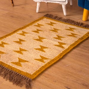 May include: A beige and mustard yellow rug with a geometric pattern of stars. The rug has fringe on all sides.