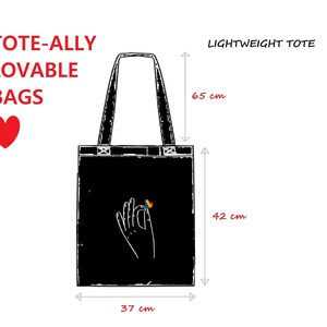 A diagram of a black lightweight tote shows its dimensions. On the bag is a simple image of a hand holding a rainbow heart.