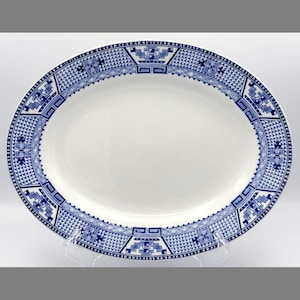 May include: An oval serving platter with a white center and a blue geometric border design. The border features repeating patterns of squares, crosses, and other shapes. The platter is made of ceramic or porcelain.