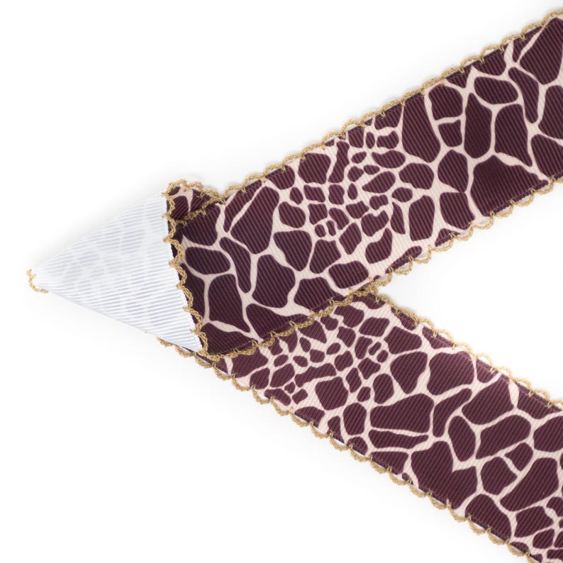 Peut inclure: Ruban d&eacute;coratif avec un imprim&eacute; girafe marron et cr&egrave;me. Le ruban a un bord festonn&eacute; avec une bordure dor&eacute;e. Le ruban est pli&eacute;, r&eacute;v&eacute;lant un dessous ray&eacute; blanc et bleu. Parfait pour les loisirs cr&eacute;atifs.