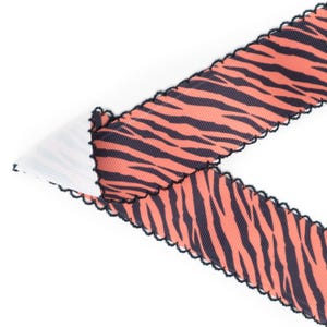 Peut inclure: Ruban d&eacute;coratif &agrave; motif de rayures de tigre en corail et bleu marine. Le ruban a un bord festonn&eacute; avec une bordure noire. Le ruban est pli&eacute; sur un tissu blanc et c&ocirc;tel&eacute;.
