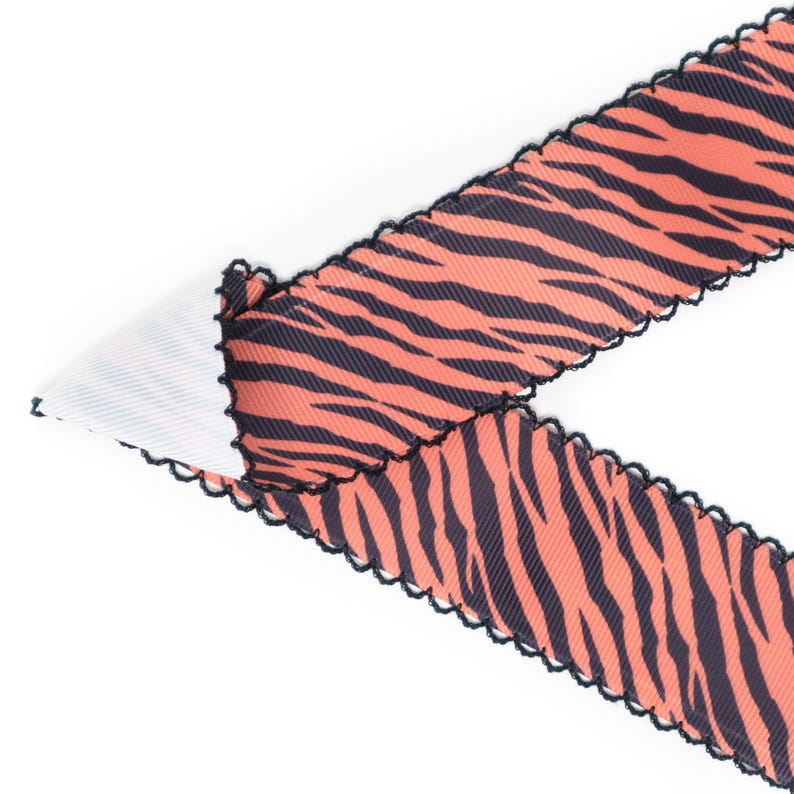 Peut inclure: Ruban d&eacute;coratif &agrave; motif de rayures de tigre en corail et bleu marine. Le ruban a un bord festonn&eacute; avec une bordure noire. Le ruban est pli&eacute; sur un tissu blanc et c&ocirc;tel&eacute;.