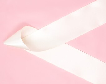 May include: A white satin ribbon tied in a loop on a pink background.
