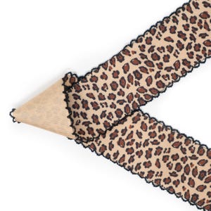 Peut inclure: Ruban beige avec un motif l&eacute;opard. Le ruban a un bord festonn&eacute; avec une bordure noire. Le ruban est pli&eacute; sur lui-m&ecirc;me, r&eacute;v&eacute;lant un dessous beige et c&ocirc;tel&eacute;. Le ruban est sur fond blanc.