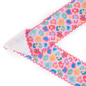 Peut inclure: Ruban rose avec un motif l&eacute;opard color&eacute;. Le ruban a un bord festonn&eacute; rose vif. L'imprim&eacute; l&eacute;opard comprend des taches bleues, jaunes, rouges et vertes.