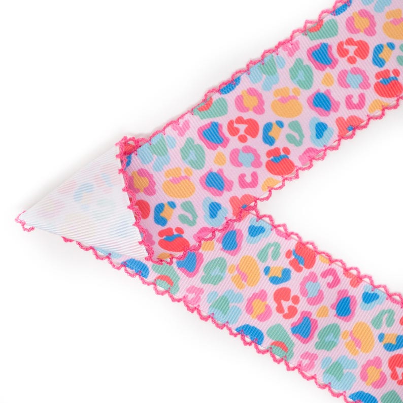 Peut inclure: Ruban rose avec un motif l&eacute;opard color&eacute;. Le ruban a un bord festonn&eacute; rose vif. L'imprim&eacute; l&eacute;opard comprend des taches bleues, jaunes, rouges et vertes.