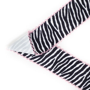Peut inclure: Ruban &agrave; imprim&eacute; z&eacute;br&eacute; noir et blanc avec une bordure festonn&eacute;e rose. Le ruban est pli&eacute;, r&eacute;v&eacute;lant un tissu ray&eacute; blanc et gris en dessous. Ce ruban d&eacute;coratif est id&eacute;al pour l'artisanat et l'emballage de cadeaux.
