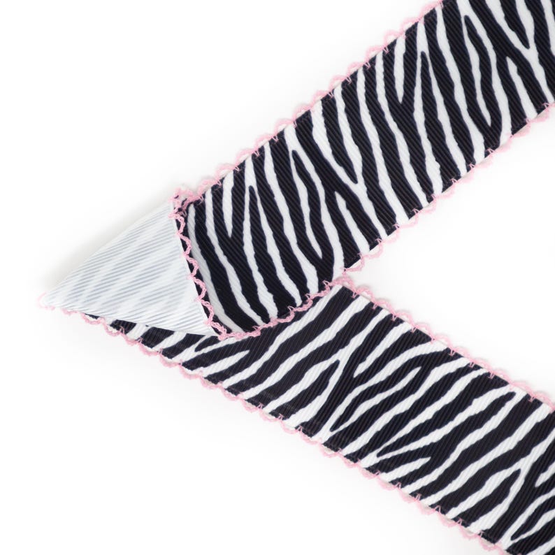 Peut inclure: Ruban &agrave; imprim&eacute; z&eacute;br&eacute; noir et blanc avec une bordure festonn&eacute;e rose. Le ruban est pli&eacute;, r&eacute;v&eacute;lant un tissu ray&eacute; blanc et gris en dessous. Ce ruban d&eacute;coratif est id&eacute;al pour l'artisanat et l'emballage de cadeaux.