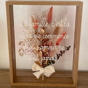 Peut inclure: Une œuvre d'art encadrée avec des fleurs séchées et une citation en français qui dit "La famille, c'est là où la vie commence et où l'amour ne finit jamais".