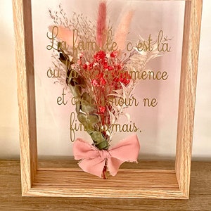 Peut inclure: Une œuvre d'art encadrée avec des fleurs séchées et un nœud rose. Le texte dans le cadre dit "La famille, c'est là où l'amour commence et où l'amour ne finit jamais."
