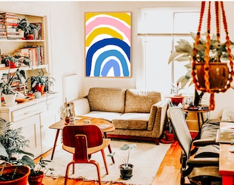 May include: A living room interior with a couch, a coffee table, a chair, and a framed abstract rainbow print on the wall. The rainbow is painted in shades of pink, yellow, blue, and light blue.