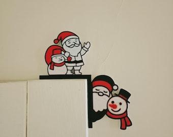 May include: Christmas-themed corner decor featuring Santa Claus and a snowman. The Santa figures wear red hats and suits with white trim. The snowman has a red scarf and a black top hat. The decor is black and white with red accents.