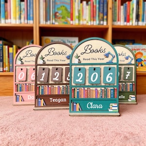May include: Wooden book counters with the text "Books Read This Year". Each counter has a bookshelf design and a flip-number display. The counters are in shades of pink, brown, and teal, with names like "Do", "Teagan", and "Clara" on them.