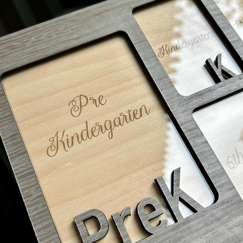 May include: A wooden photo frame with spaces for multiple pictures. The frame is gray and has the word "Prek" cut out at the bottom. The words "Pre Kindergarten" and "Kindergarten" are engraved on the wooden surface.