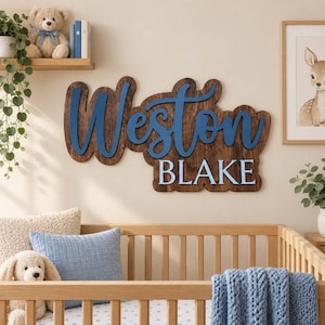 May include: A custom wooden wall sign featuring the name Weston in a blue cursive script layered over a dark brown wood backing, with the name BLAKE in light blue block letters underneath, creating a dimensional name plaque for wall display.
