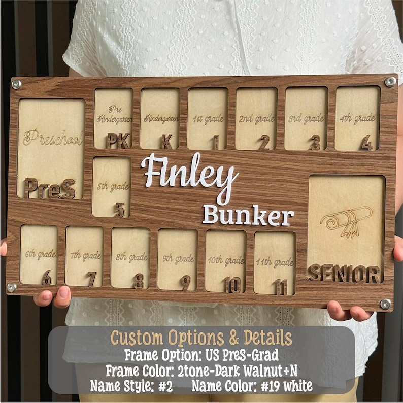 May include: A personalized wooden school years display board with spaces for photos from preschool through senior year. The name "Finley Bunker" is prominently displayed in white, with grade levels labeled 1st through 11th grade.