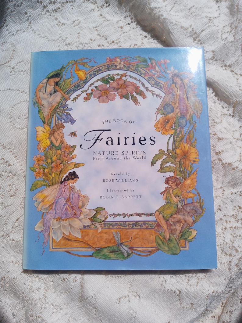 Puede incluir: Un libro de tapa dura titulado "The Book of Fairies" con una cubierta azul claro. La cubierta presenta ilustraciones de hadas, flores y el texto "Nature Spirits From Around the World". El libro est&aacute; narrado por Rose Williams e ilustrado por Robin T. Barrett.