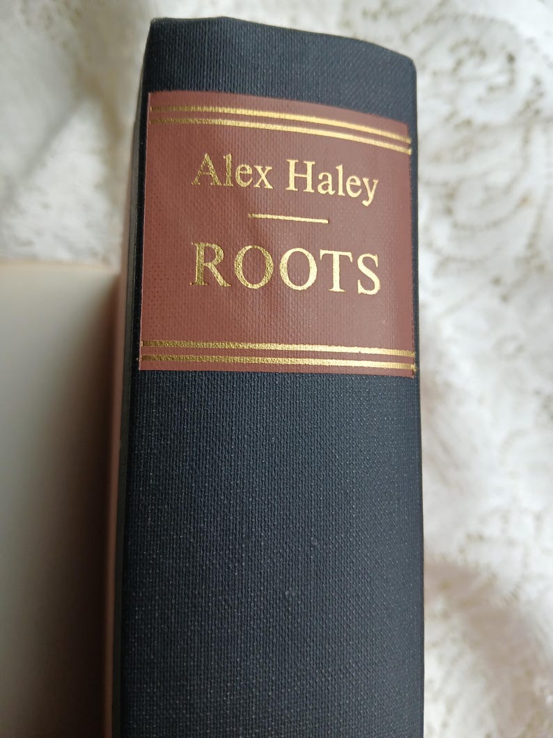 May include: A hardcover book titled "Roots" by Alex Haley. The book has a dark blue cover with a brown label featuring gold lettering. The title and author's name are prominently displayed.