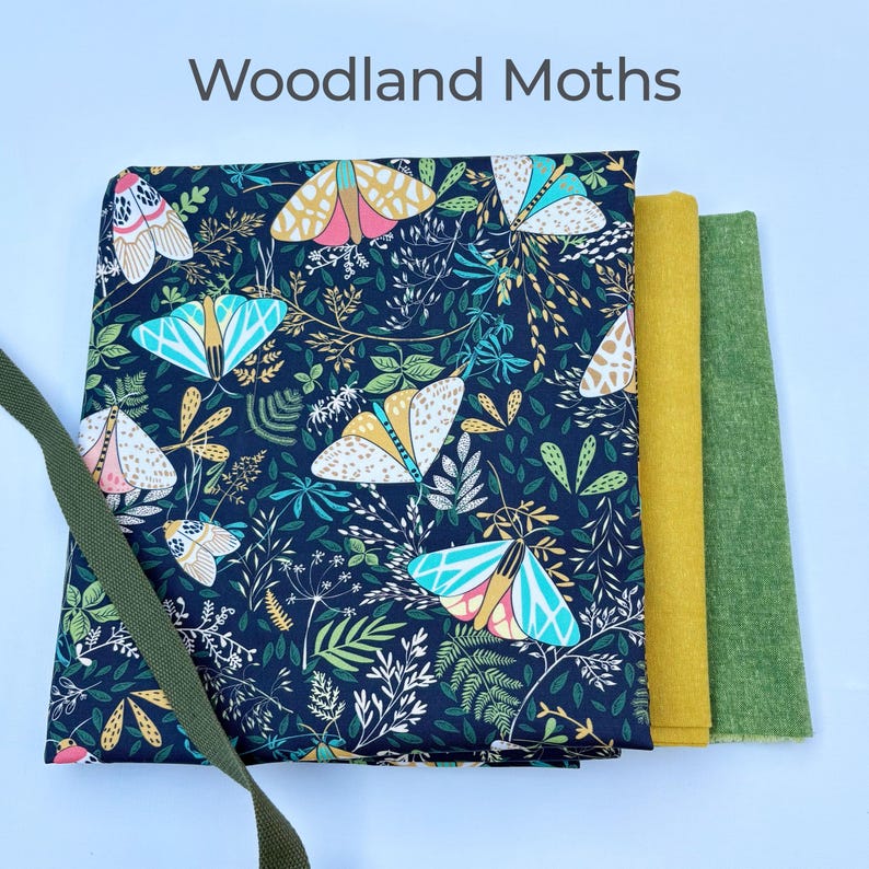 Może przedstawiać: Ciemnoniebieska tkanina z powtarzającym się wzorem kolorowych motyli i liści. U g&oacute;ry napis "Woodland Moths". Obok tkaniny znajdują się dwie pr&oacute;bki tkanin w jednolitym kolorze, jedna w kolorze musztardowym, druga zielona. Zielony pasek po lewej stronie.