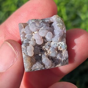 May include: A close-up of a gray and purple agate with a unique, bubbly texture. The agate is a natural stone with a variety of colors and patterns.