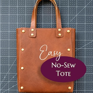 May include: A brown leather tote bag featuring two vertical handles and gold-toned metal rivets along the sides. The front of the bag displays the white text Easy and a dark purple oval overlay with the white text NO-SEW TOTE printed on it.