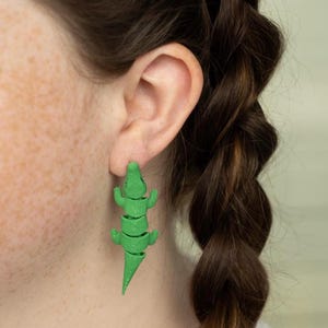 May include: Green alligator earrings. The alligator is segmented and appears to be made of plastic.