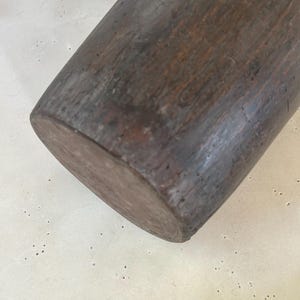 K&ouml;nnte beinhalten: Ein zylindrisches Nudelholz aus Holz mit dunkelbraunem Finish und sichtbarer nat&uuml;rlicher Holzmaserung. Die Oberfl&auml;che weist Gebrauchsspuren und Alterungserscheinungen mit kleinen Vertiefungen und Farbvariationen &uuml;ber die gesamte L&auml;nge auf.