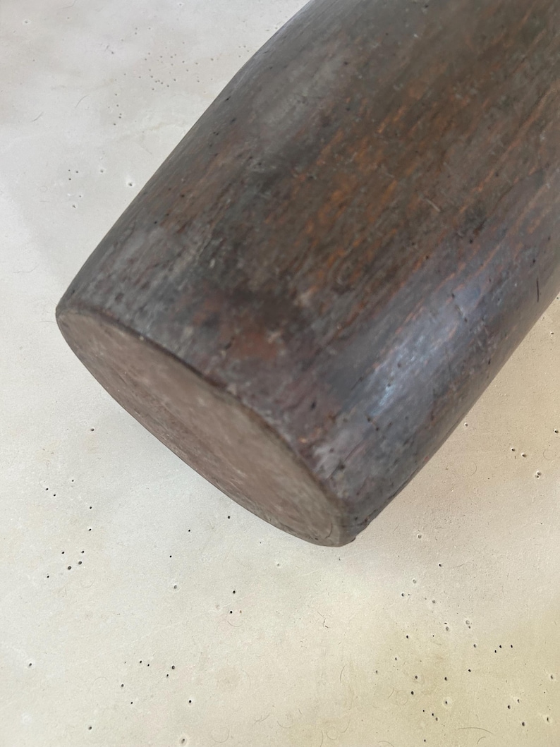 K&ouml;nnte beinhalten: Ein zylindrisches Nudelholz aus Holz mit dunkelbraunem Finish und sichtbarer nat&uuml;rlicher Holzmaserung. Die Oberfl&auml;che weist Gebrauchsspuren und Alterungserscheinungen mit kleinen Vertiefungen und Farbvariationen &uuml;ber die gesamte L&auml;nge auf.