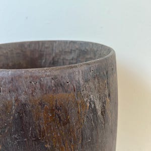 K&ouml;nnte beinhalten: Ein zylindrisches Gef&auml;&szlig; aus dunkelbraunem Holz mit einer verwitterten, strukturierten Oberfl&auml;che. Die Au&szlig;enseite zeigt sichtbare Maserungen, kleine Vertiefungen und ein raues Finish, w&auml;hrend das Innere eine tiefe, dunkle H&ouml;hlung aufweist.