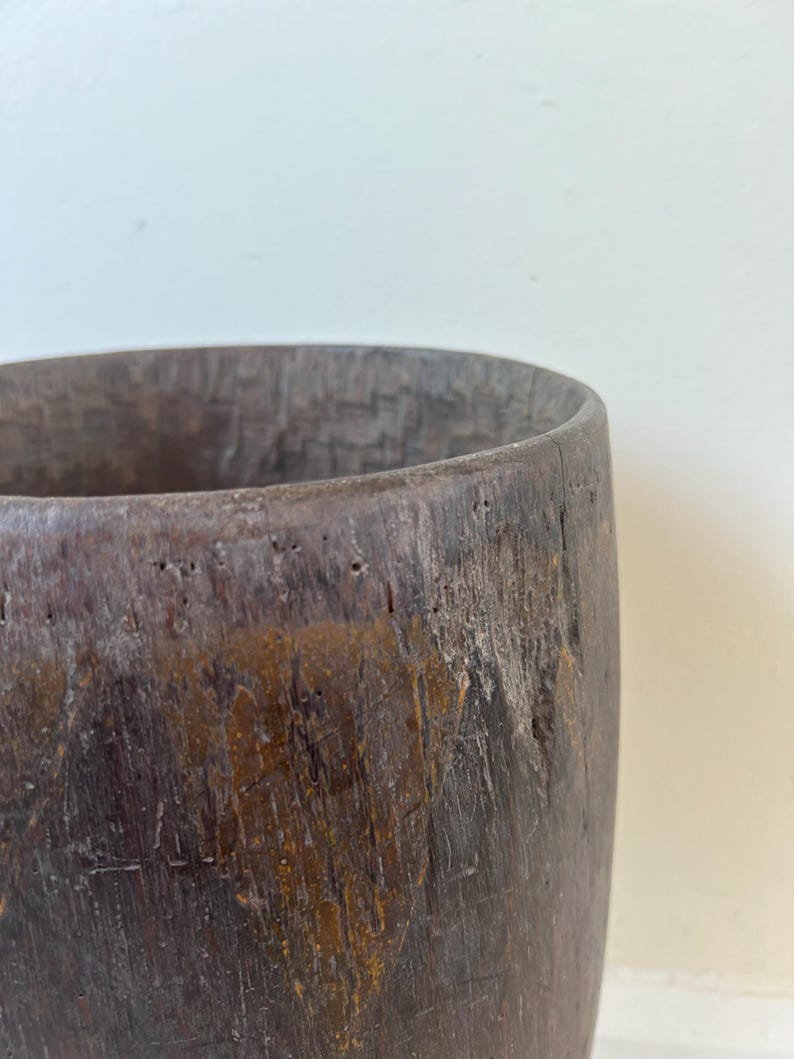 K&ouml;nnte beinhalten: Ein zylindrisches Gef&auml;&szlig; aus dunkelbraunem Holz mit einer verwitterten, strukturierten Oberfl&auml;che. Die Au&szlig;enseite zeigt sichtbare Maserungen, kleine Vertiefungen und ein raues Finish, w&auml;hrend das Innere eine tiefe, dunkle H&ouml;hlung aufweist.