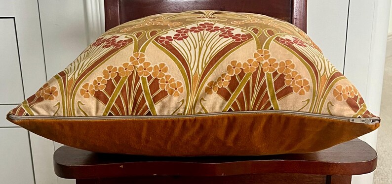 Puede incluir: Coj&iacute;n decorativo con un estampado floral en tonos beige, marr&oacute;n y rojo. Tiene una base de terciopelo marr&oacute;n y un cierre de cremallera. El dise&ntilde;o presenta flores y hojas estilizadas.