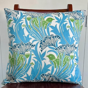 Puede incluir: Cojín decorativo cuadrado con un estampado floral en tonos azules, verdes y blancos. El diseño presenta flores y hojas estilizadas, creando un tema inspirado en la naturaleza. El cojín está colocado sobre una silla de madera.