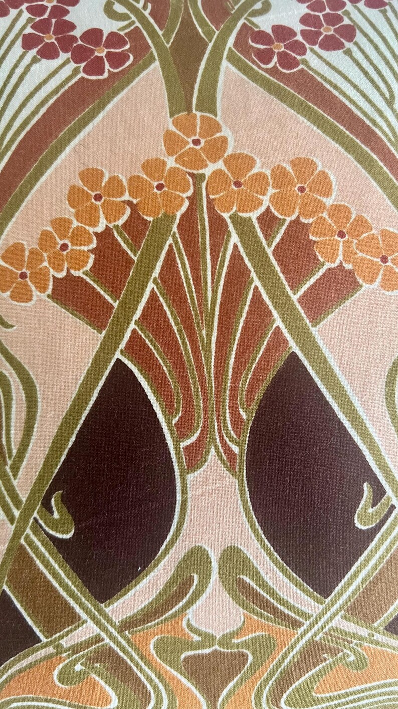 Puede incluir: Primer plano de una tela con un dise&ntilde;o floral Art Nouveau. El patr&oacute;n presenta flores estilizadas en tonos naranja, marr&oacute;n y burdeos, sobre un fondo rosa claro y crema. Los tallos verdes y las l&iacute;neas curvas completan el dise&ntilde;o.