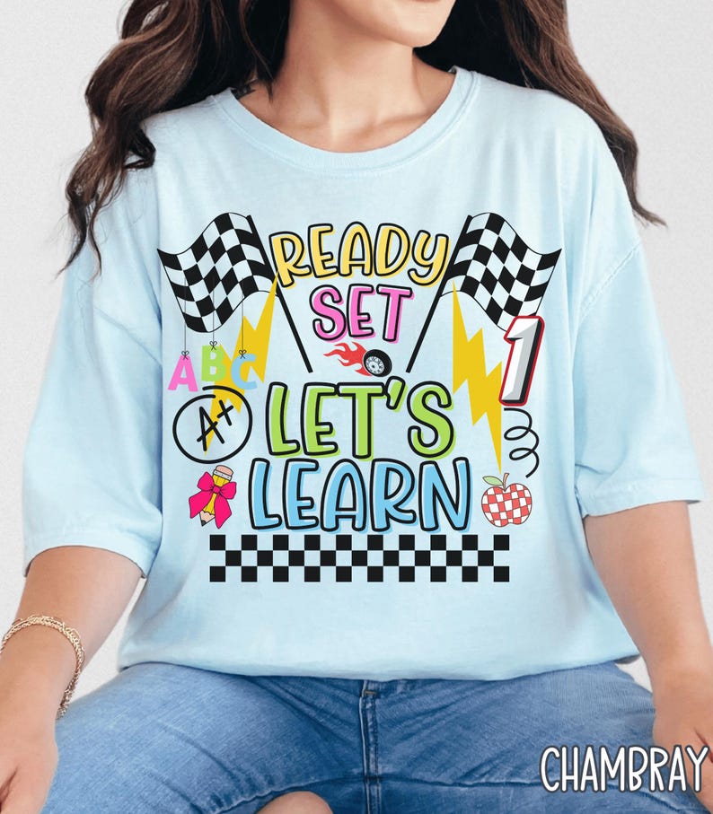 May include: Light blue t-shirt with the text "READY SET LET'S LEARN" in yellow, pink, and green. The design includes checkered flags, lightning bolts, and a race car wheel. A number 1 is also featured in the design.
