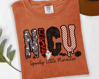 以下が含まれることがあります： 錆色のTシャツで、NICUの文字がゴースト、カボチャ、ヒョウ柄、クモの巣、チェック模様などの様々なパターンで描かれたグラフィックプリントが施されています。文字の下にはSpooky Little Miraclesというテキストがあります。