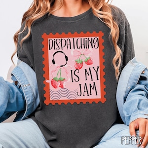 May include: Dark gray sweatshirt featuring a postage stamp design with the text "Dispatching Is My Jam." The stamp includes a headset, strawberries, and pink bows. The sweatshirt is a comfortable, casual style.