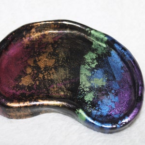 May include: A black resin dish with a rainbow iridescent finish. The dish has a unique kidney bean shape and is perfect for holding small items.