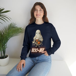 May include: A navy blue sweatshirt with a white ghost holding a pumpkin and a cup. The text "BOO-JEE" is printed in orange below the ghost.