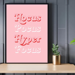 May include: A pink printable wall art print with the text "Hocus Pocus Hyper Focus" in red and white letters.