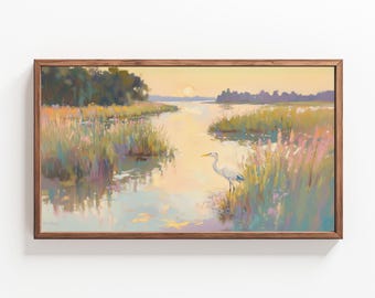 May include: A framed pastel painting of a white egret standing in a marsh at sunset. The water is calm and reflects the sky, which is a soft orange and pink. The egret is facing to the right, with its head turned to the left. The marsh is filled with tall grasses and reeds.