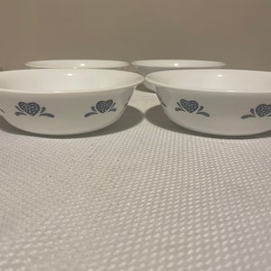 Peut inclure: Quatre bols en céramique blanche avec un motif floral bleu et blanc. Les bols sont disposés en rangée sur une surface blanche.
